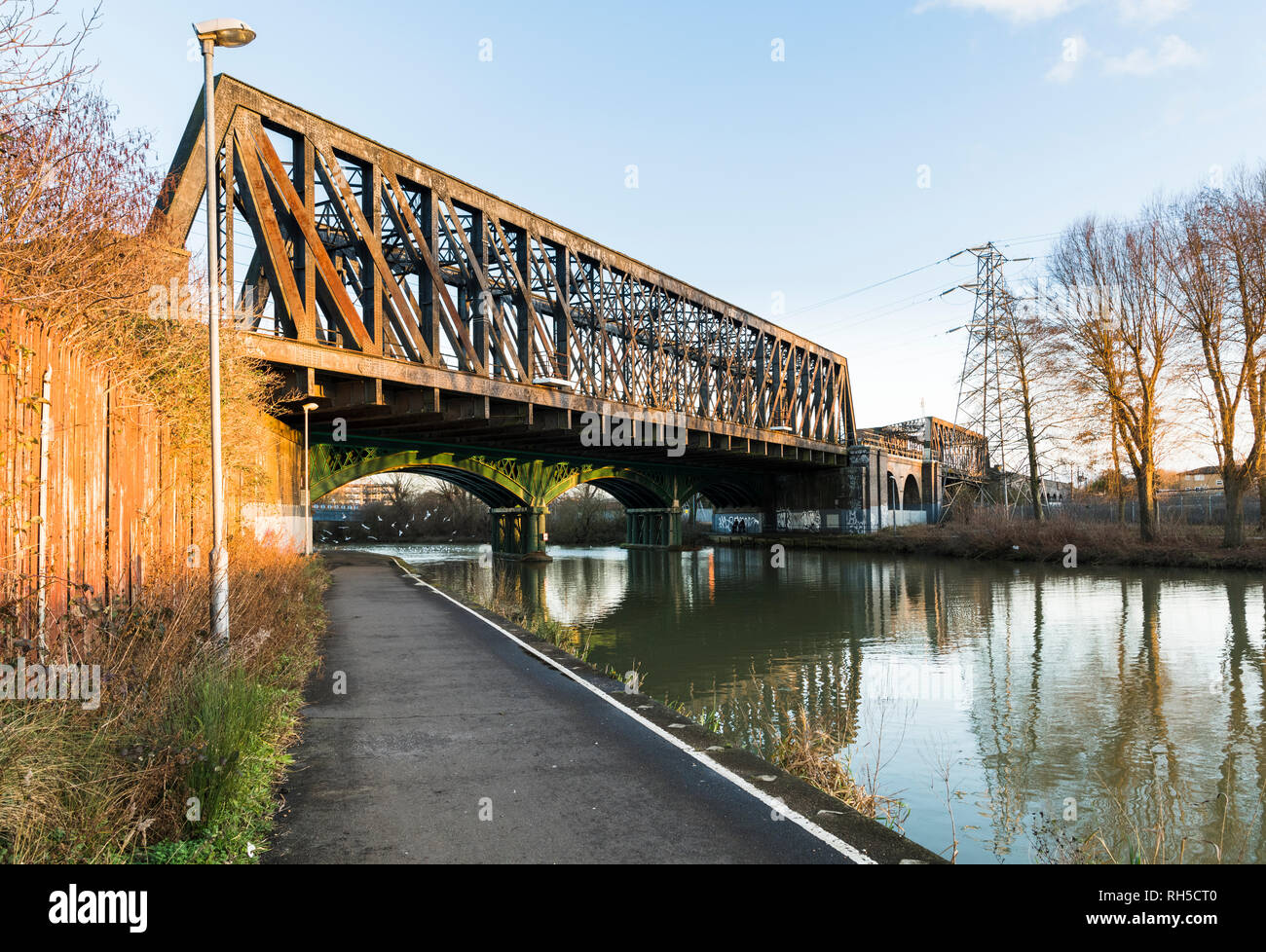 Path beside River Nene in central Peterborough, Cambridgeshire, with 19th century cast iron railway bridge, still in use on the East Coast Mainline Stock Photo