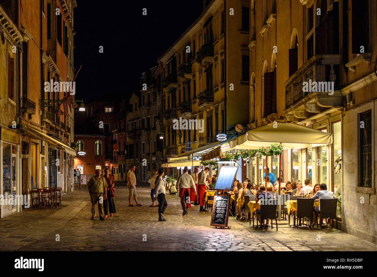 Tourists walking by a busy restaurant terrace in the Cannaregio district of Venice at night Stock Photo