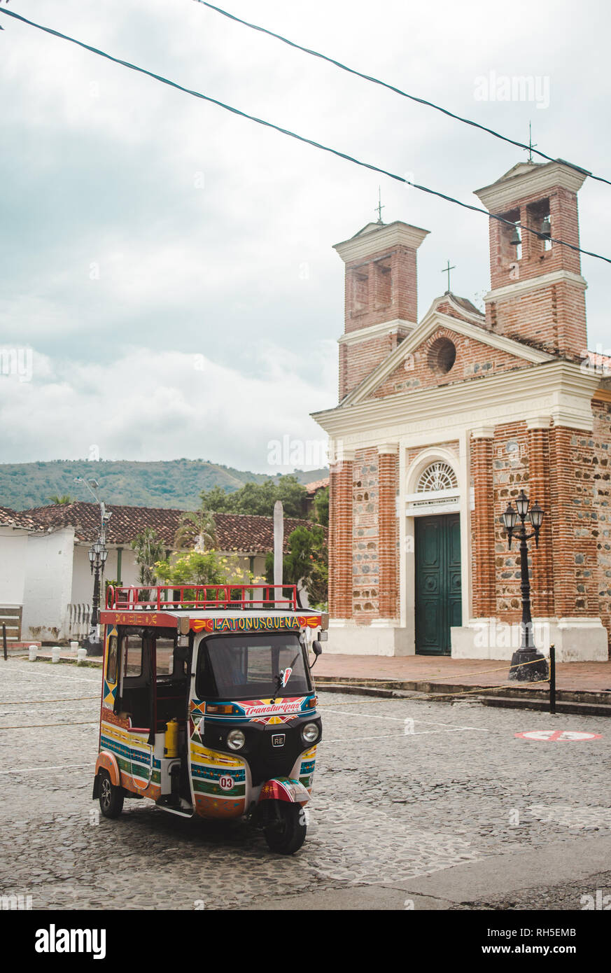 Colorfully painted tuktuk sits outside brick chapel in the typical Colombian town of Santa Fe de Antioquia near Medellín, Colombia Stock Photo