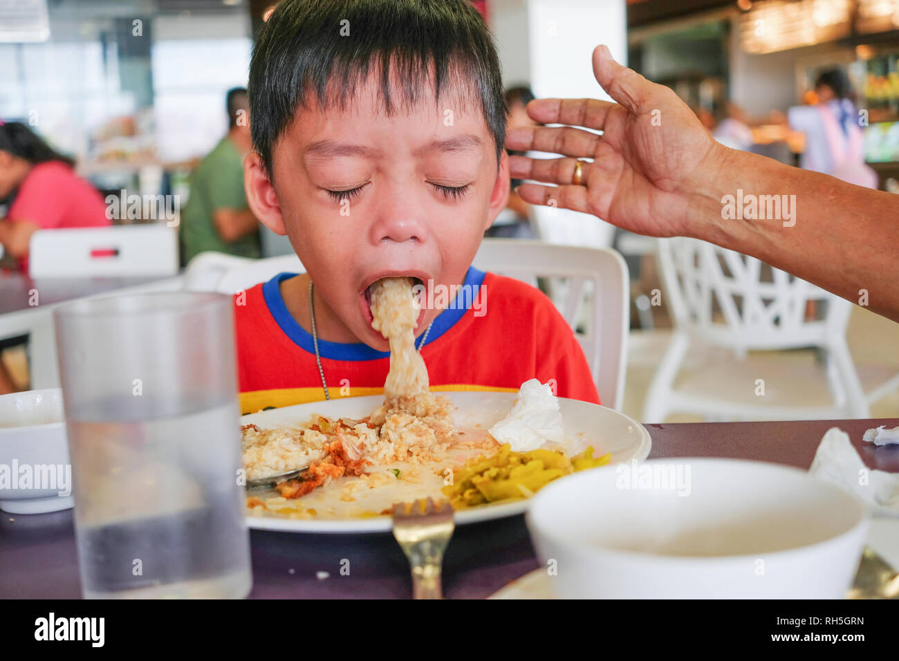 Boy puking on plate after having lunch meal in food court with helping hand Stock Photo