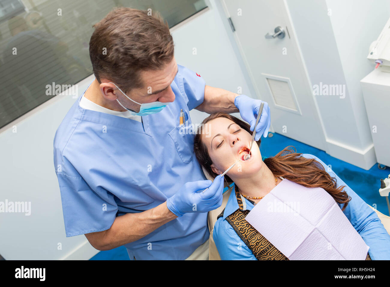 Dentist performing teeth treatment with female patient open mouth with