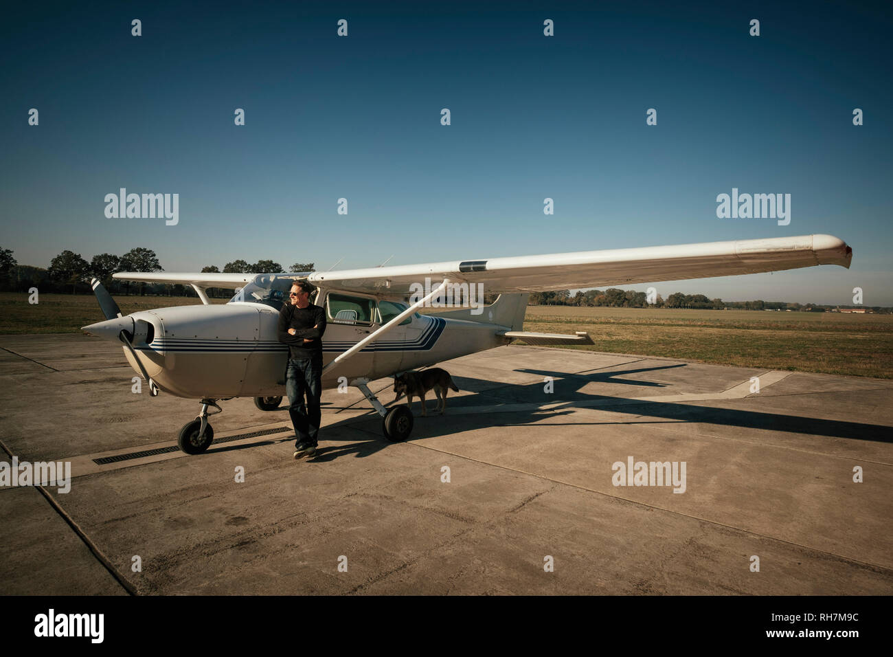Male pilot standing at small propellor airplane on sunny tarmac Stock Photo