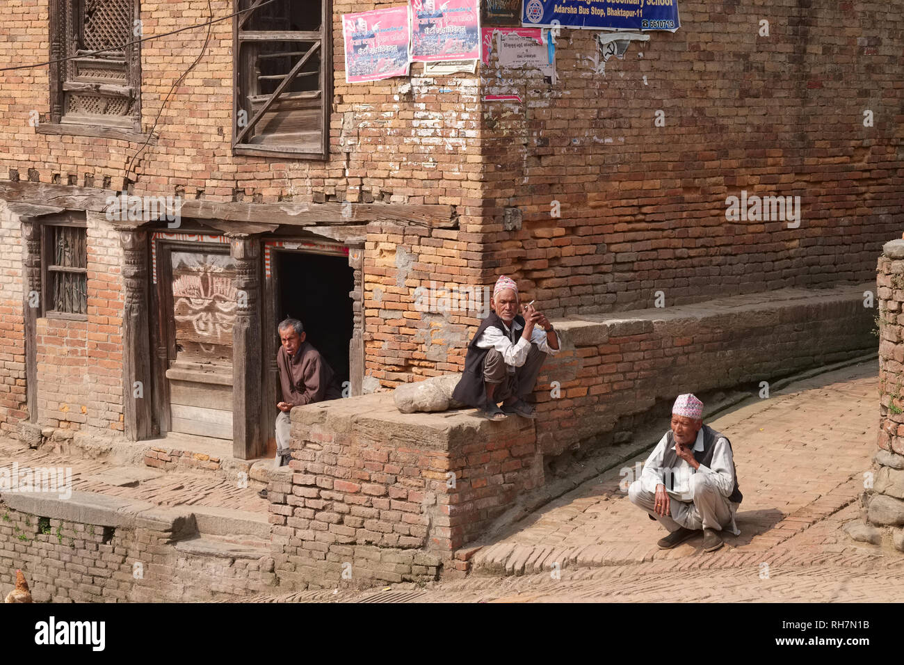 Men of the Newar community in traditional attire, including Nepalese topi (cap),  watching the world go by, Bhaktapur, Kathmandu Valley, Nepal Stock Photo