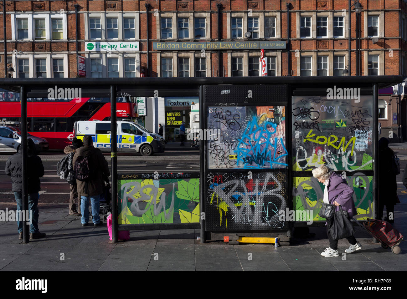 An elderly lady struggles with her shopping trolley past a graffiti-covered bus stop in Brixton, on 30th january 2019, in Lambeth, south London, England. Stock Photo