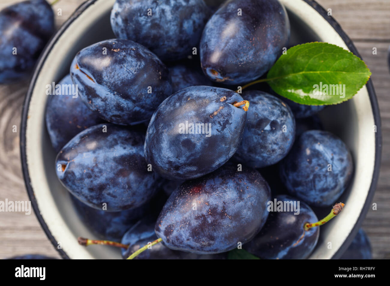 Top view of a bowl full of ripe prune fruit on a wooden table, close-up Stock Photo