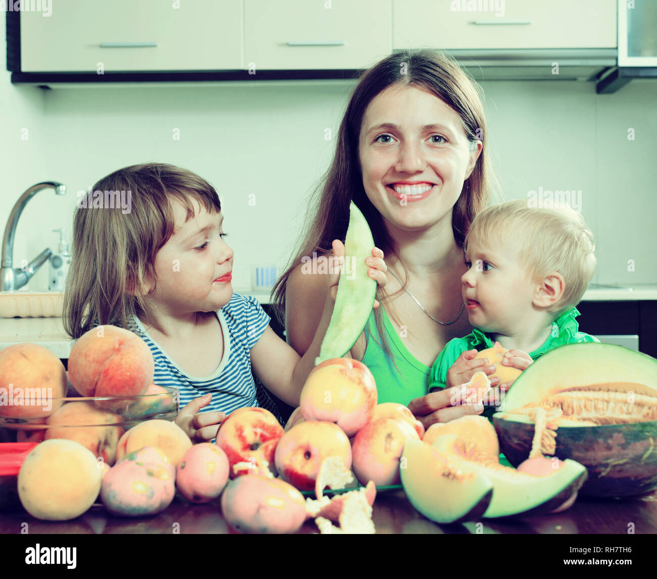 Happy woman with daughters eating melon and peaches at home Stock Photo