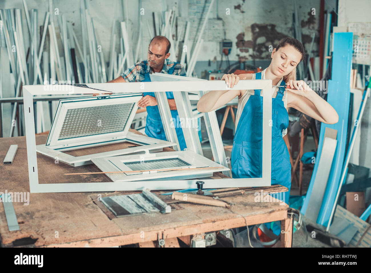 Efficient positive  workwoman assembling PVC window in workshop with manual tools Stock Photo