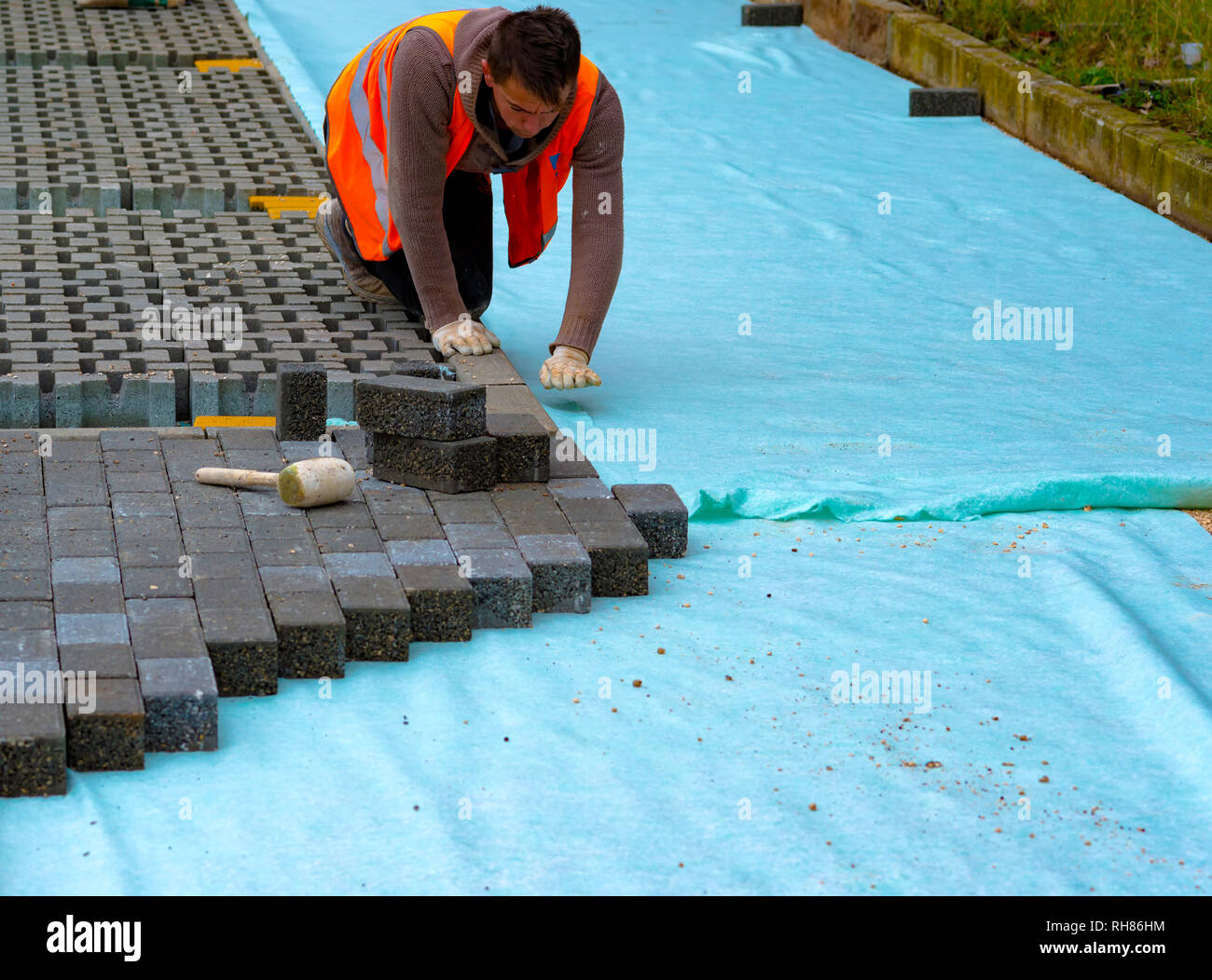 Construction worker laying interlocking paving concrete onto sheet
