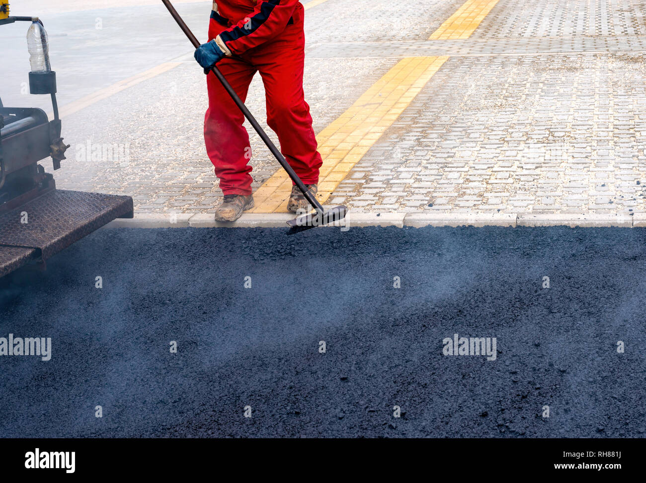 Worker distributes on the edge the asphalt laid out for the construction of a road Stock Photo