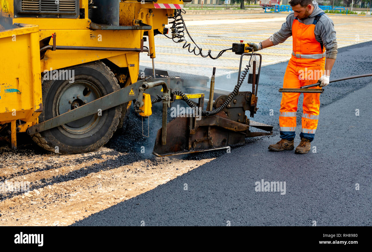Workers regulate tracked paver laying asphalt heated to temperatures above 160 ° pavement on a runway Stock Photo