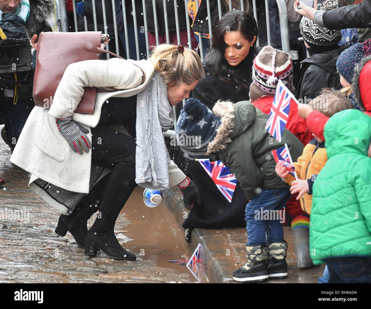 An aide (left) lifts the coat of the Duchess of Sussex out of a puddle as she speaks to children at a visit to the Bristol Old Vic theatre, which is undergoing a multimillion-pound restoration. Stock Photo