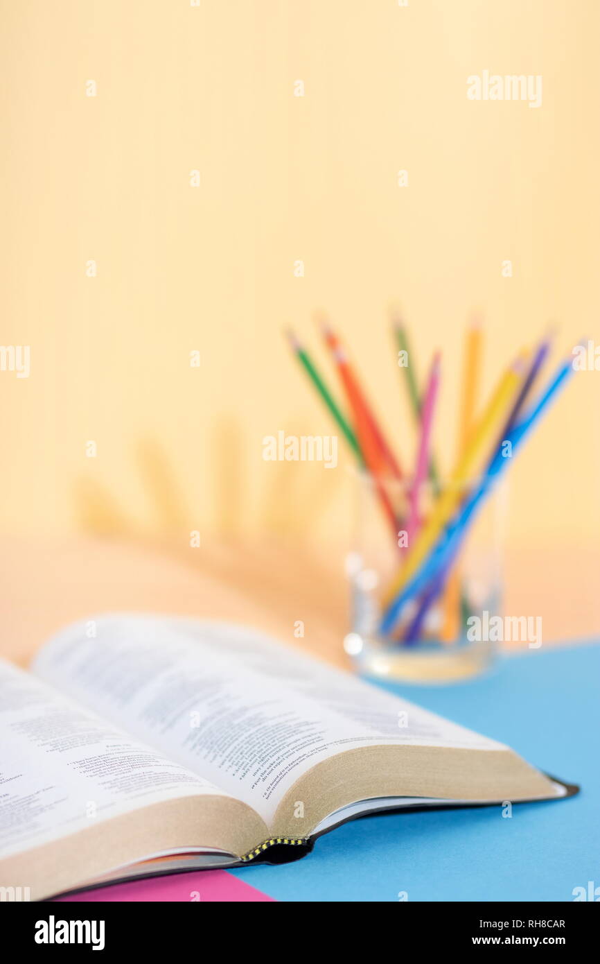Bible book and glass with a set of colored pencils on a colored paper background ready to be studied and underlined. Ready for Bible study. Stock Photo