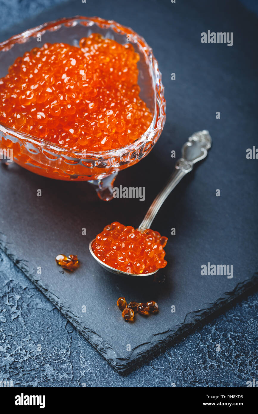 Salmon red caviar in crystal plate with spoon on black background. Exquisite delicacy Stock Photo