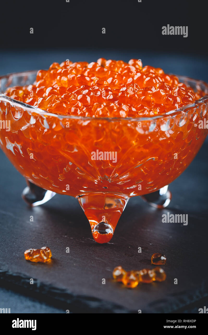 Salmon red caviar in crystal plate with spoon on black background. Exquisite delicacy Stock Photo