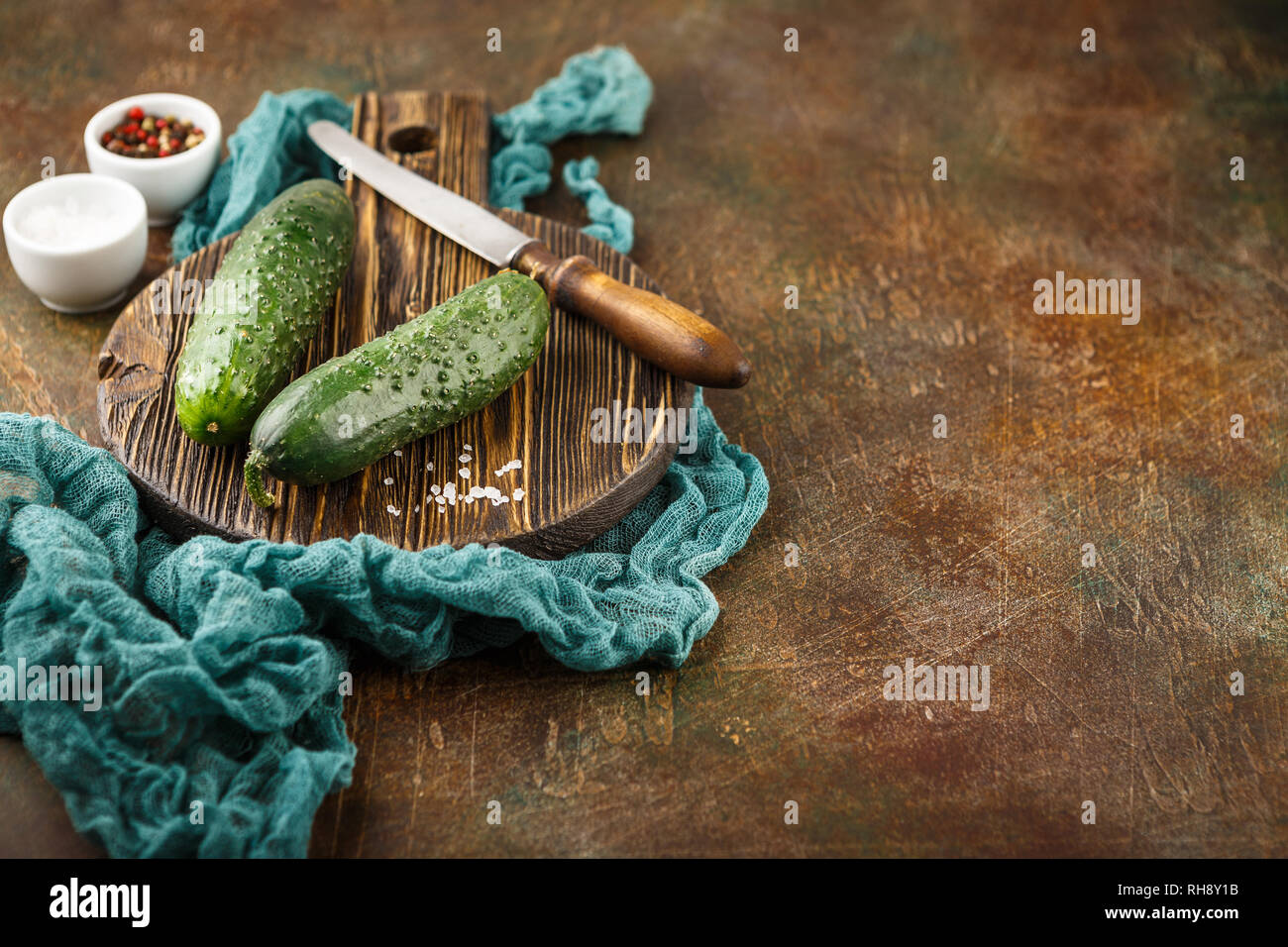 Fresh cucumber, old knife, salt and pepper on wooden board. Space for text. Stock Photo