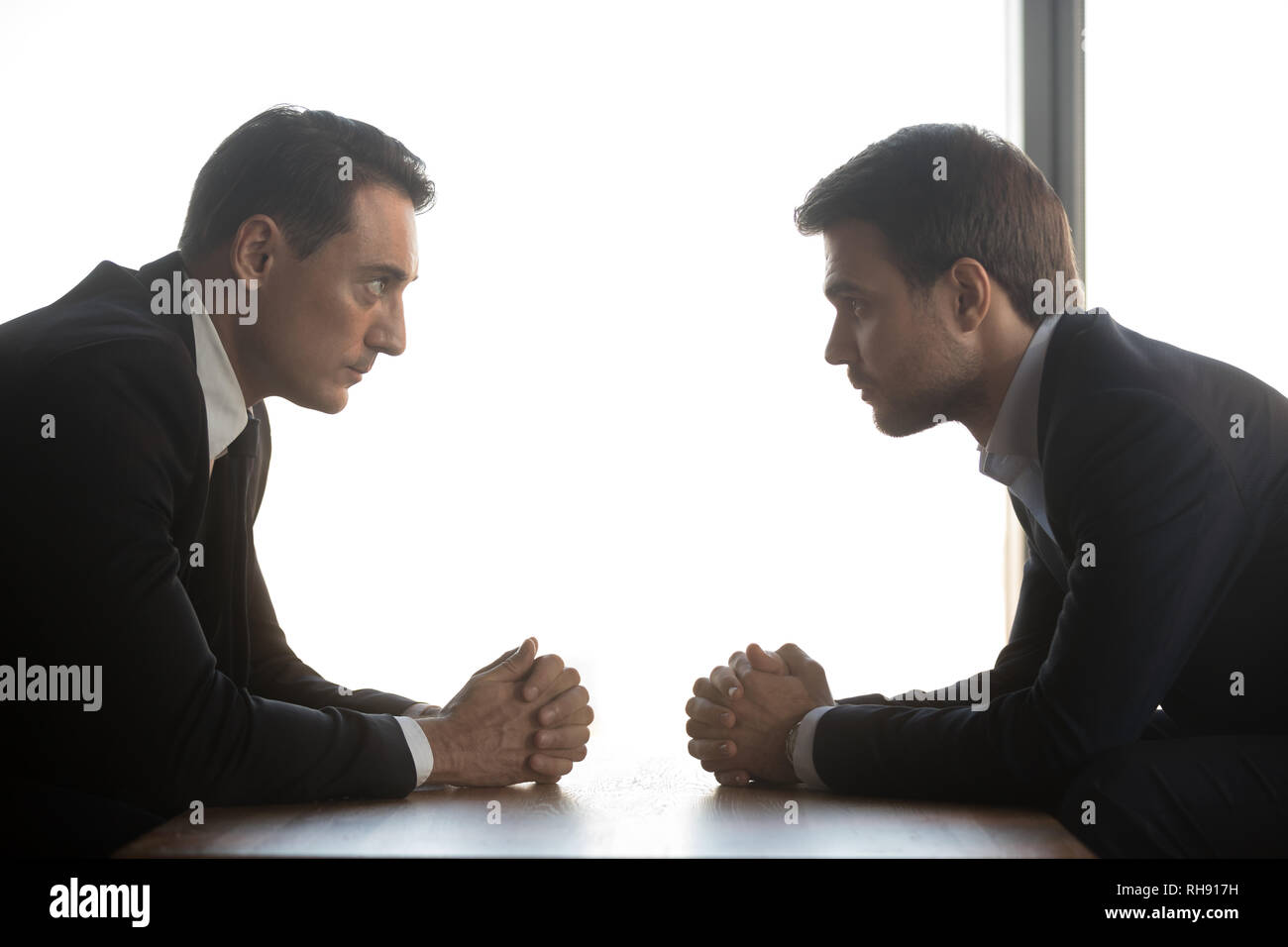 Two businessmen look at each other sitting opposite, rivalry concept Stock Photo