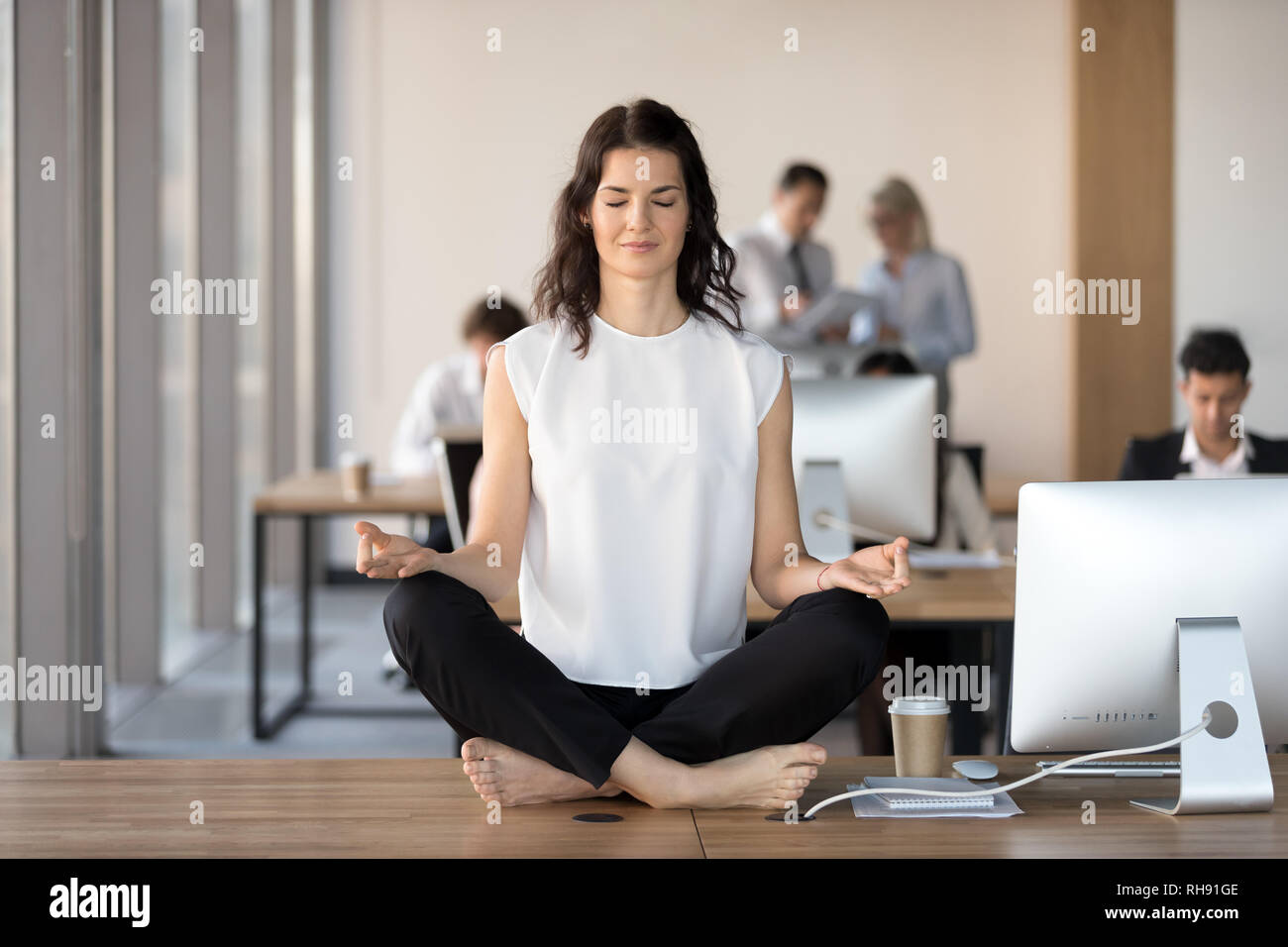 Calm Young Businesswoman Doing Yoga Exercise At Work Desk Stock