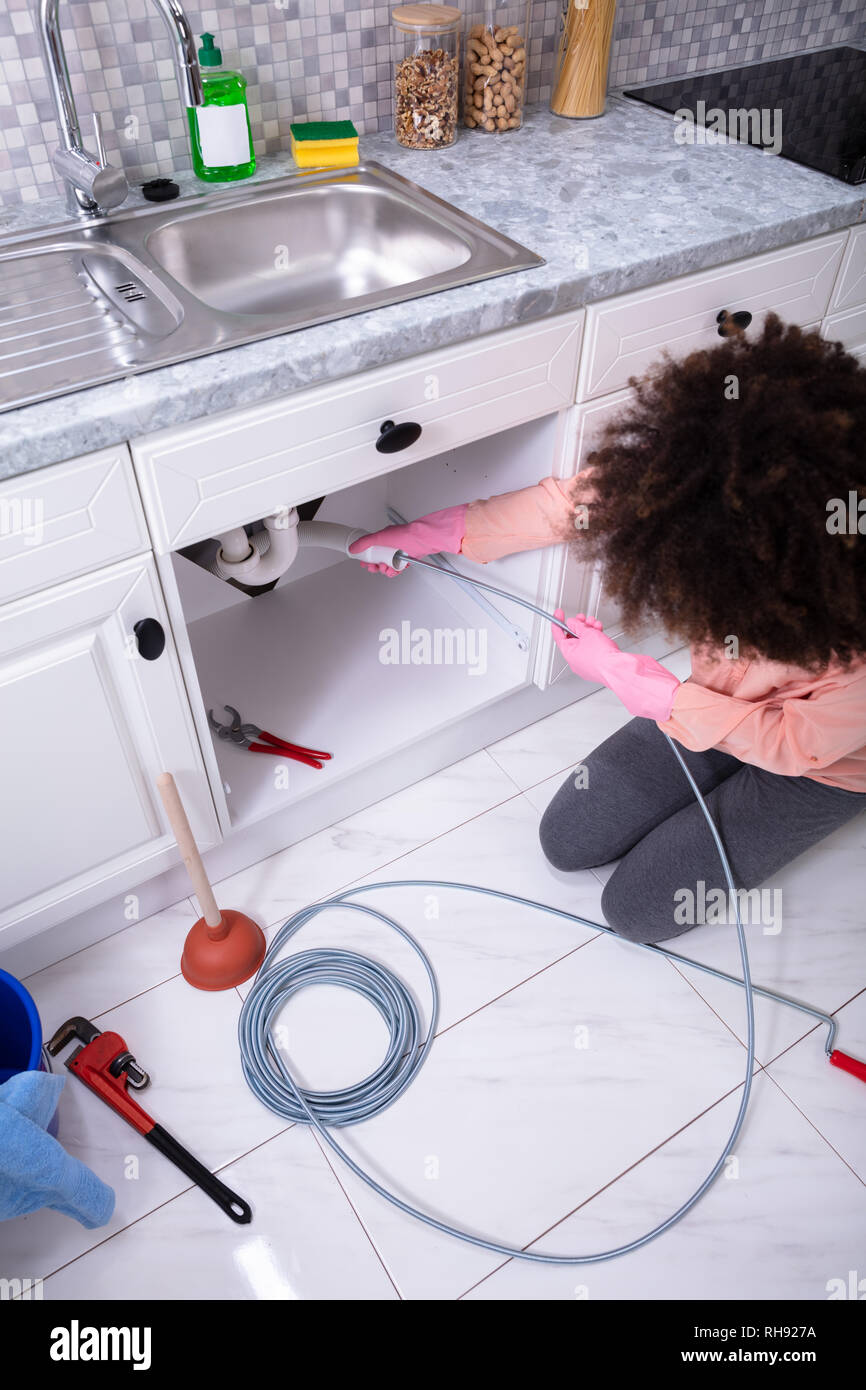 A Young Woman Cleaning Clogged Sink Pipe With Drained Cable
