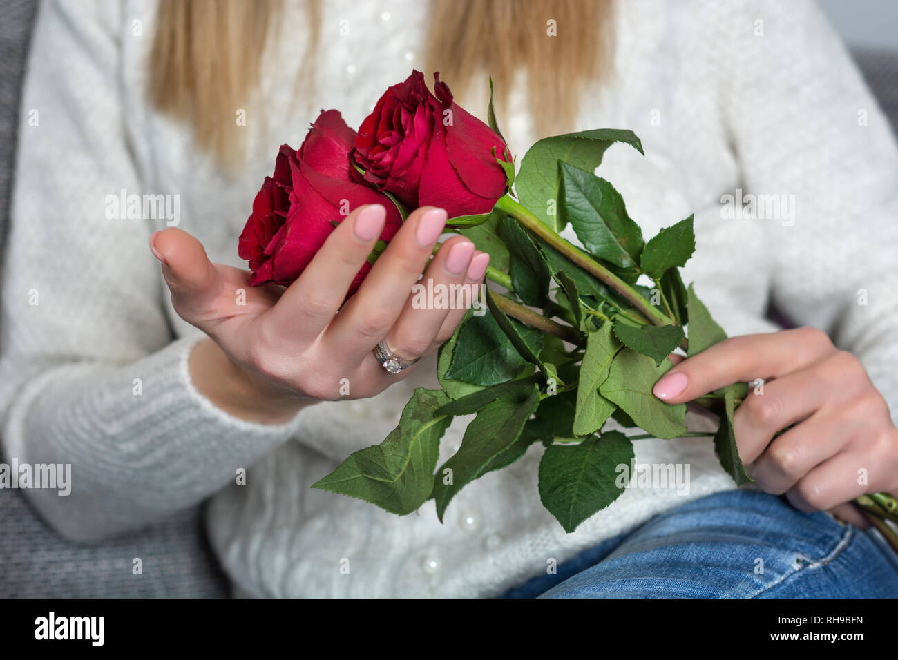 Young woman holding beautiful red rose in hands and sitting in bed ...