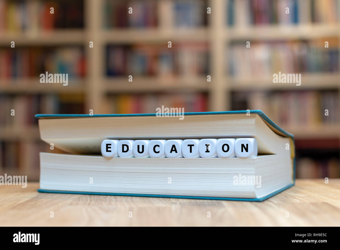 Dice in a book form the word 'EDUCATION'. Book is lying on a wooden table in a library. Stock Photo