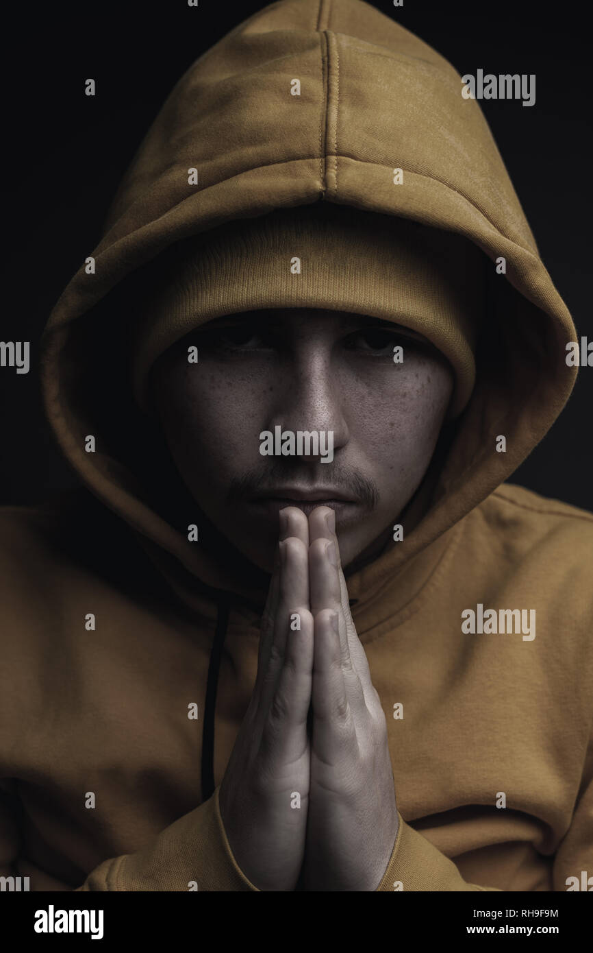 low key portrait of young rapper with yellow hoodie and praying hands Stock Photo