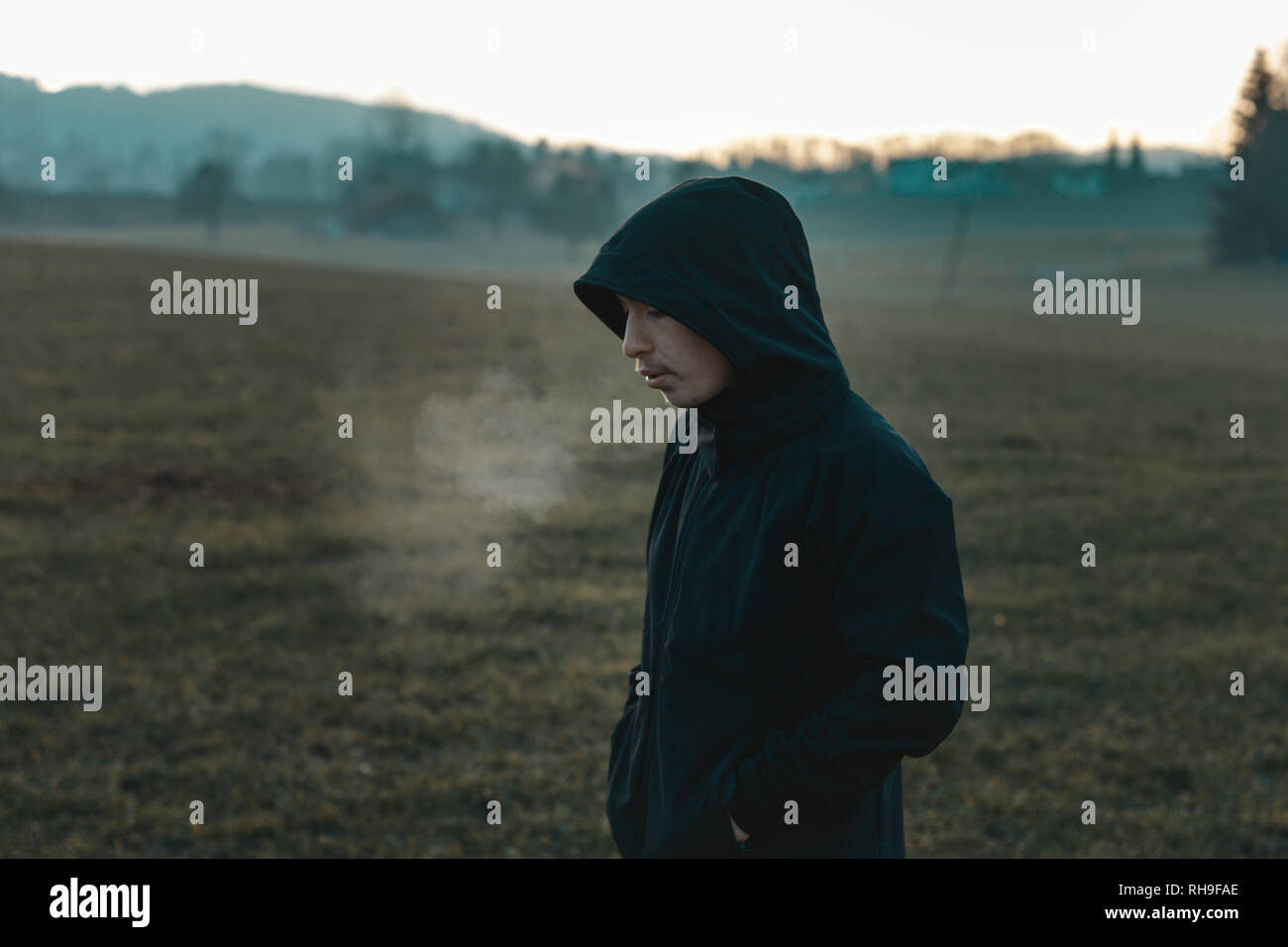thinking teen with hoodie standing outside at field and breathe out Stock Photo