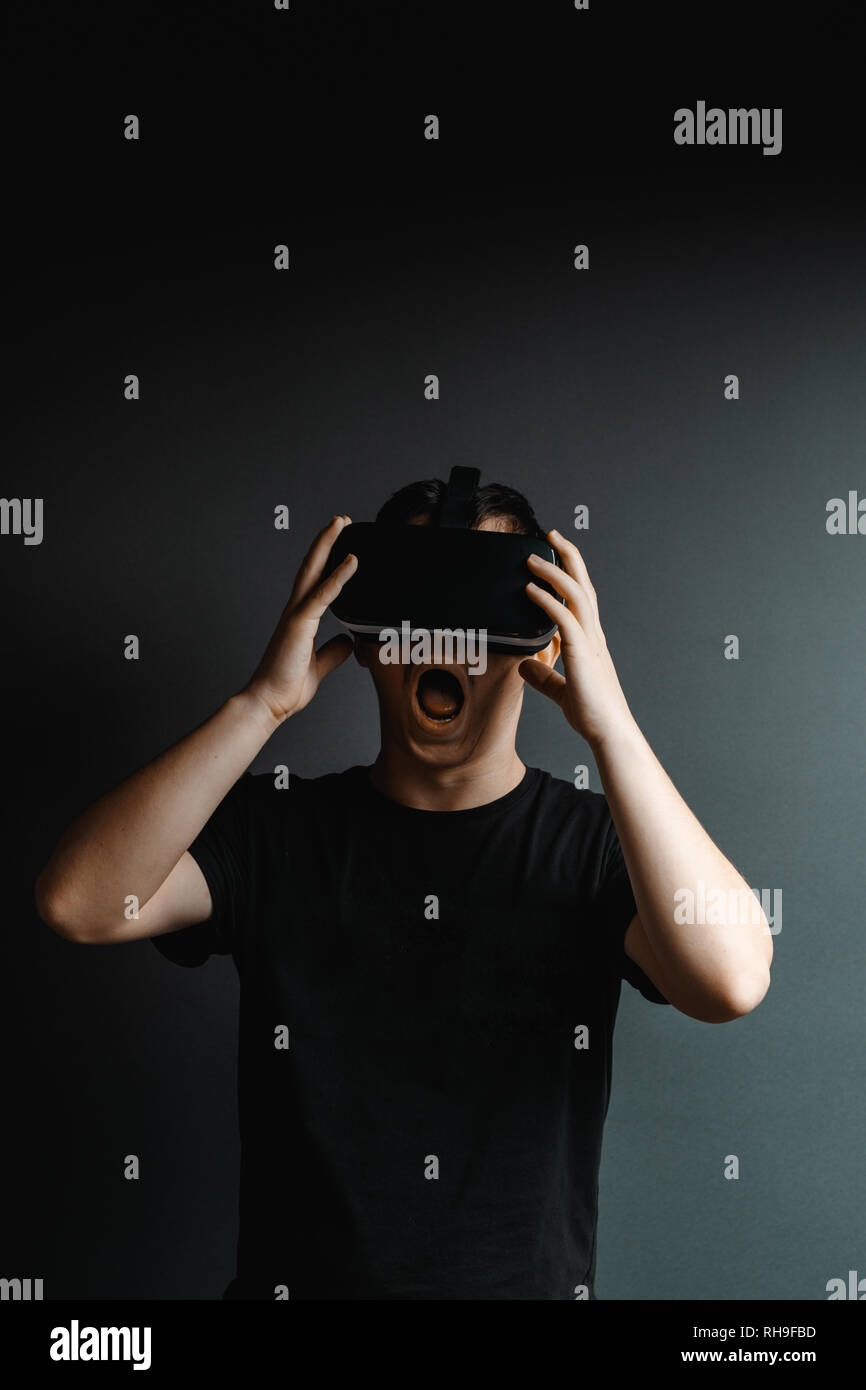Portrait of scary young man getting experience with vr device playing horror game in front of grey background. Stock Photo