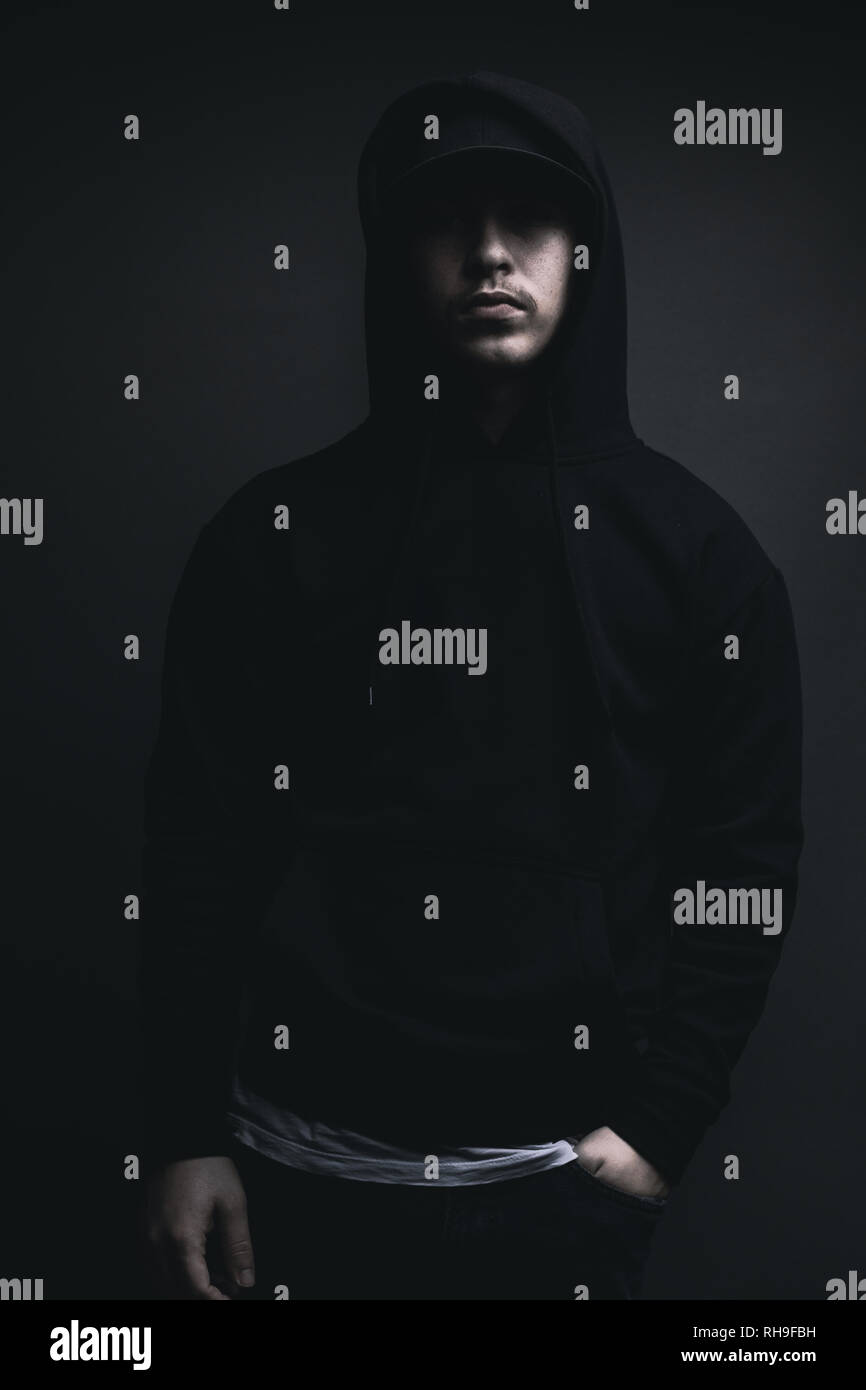 young cool rapper with black hoodie and cap standing in front of grey background Stock Photo