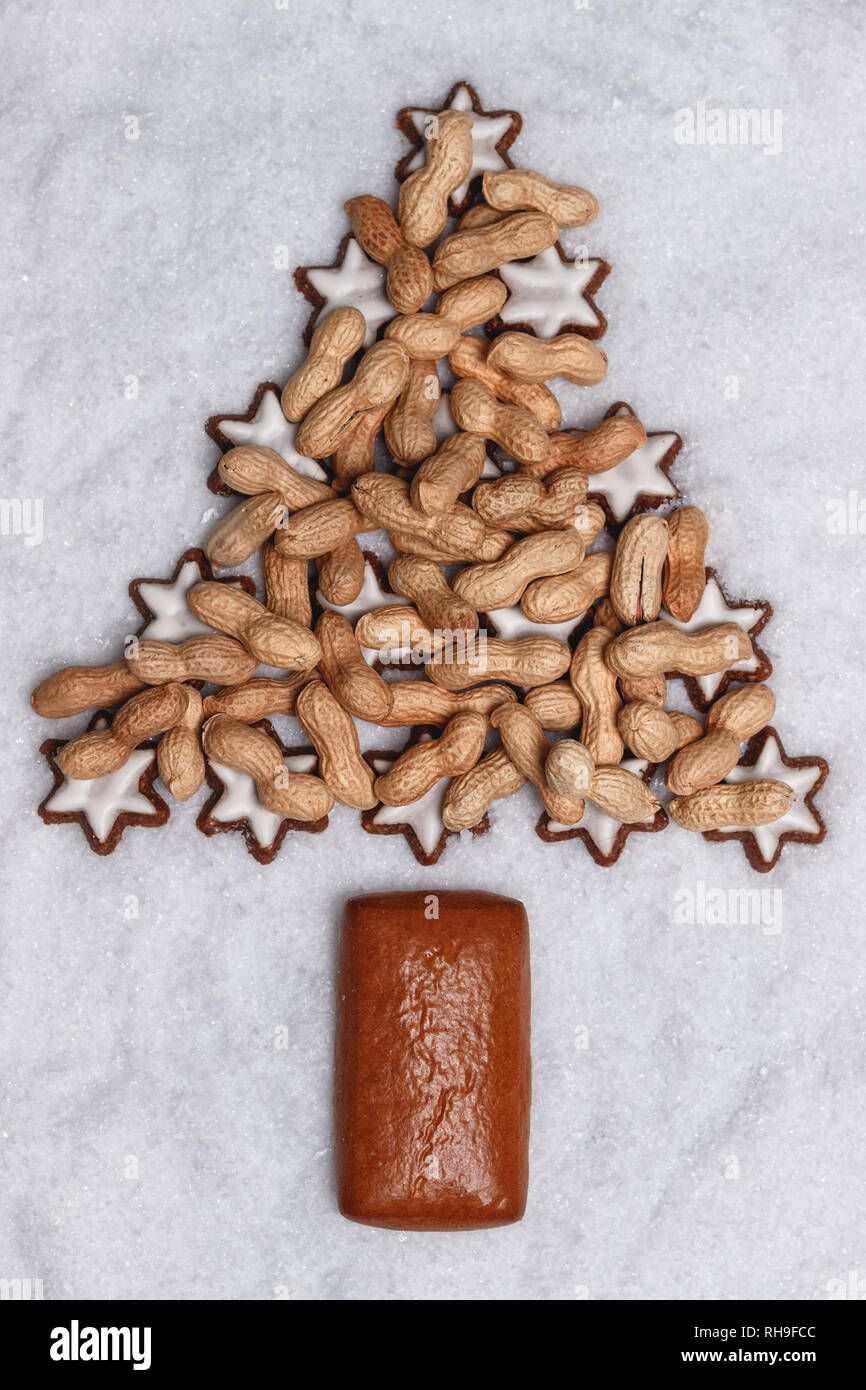 cinnamon stars and gingerbread with christmas nuts laying on snow and form a fir tree Stock Photo