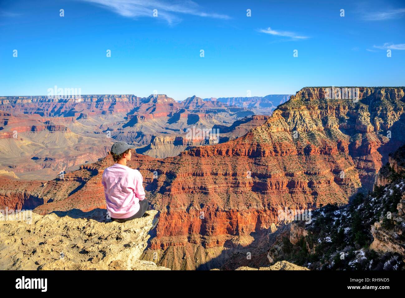 Young woman looking into the distance, sitting at the precipice of the gigantic gorge of the Grand Canyon, view from the Rim Stock Photo