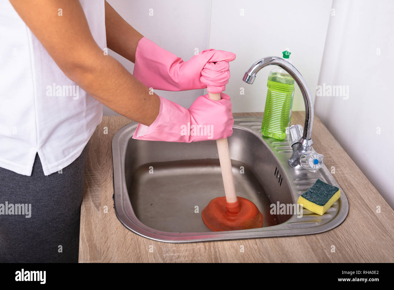 Close-up Of A Female Plumber Wearing Pink Gloves Using Plunger In The Kitchen Sink Stock Photo