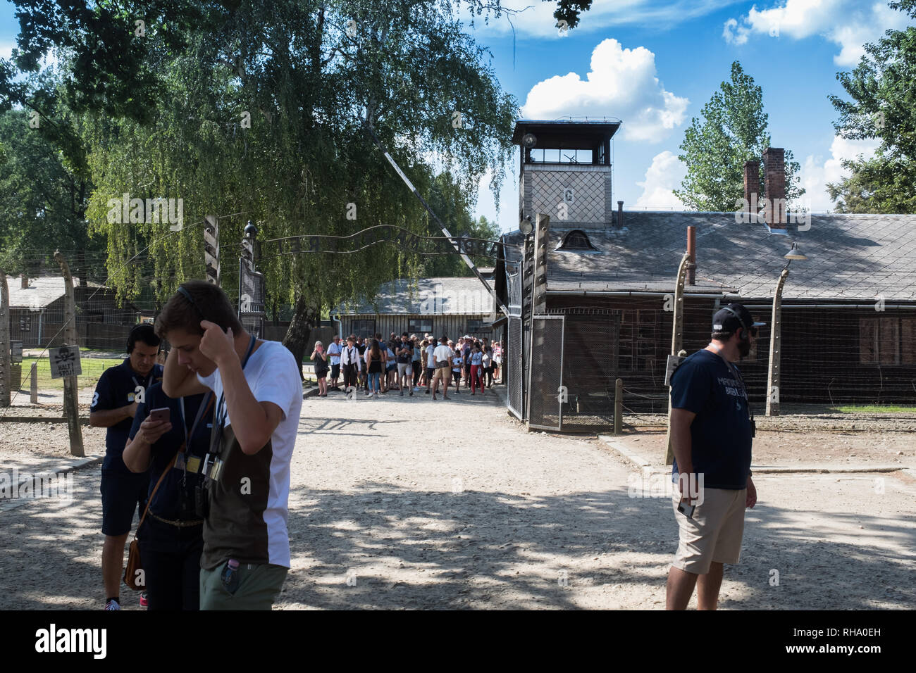 Tourists listening to tour guide on headphones at gate at Birkenau -Auschwitz Stock Photo