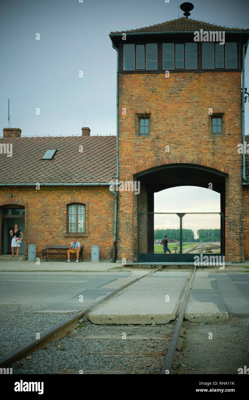 Railway lines leading inside from the main entrance at Birkenau (Auschwitz II - Birkenau) with tourists smoking outside. Stock Photo