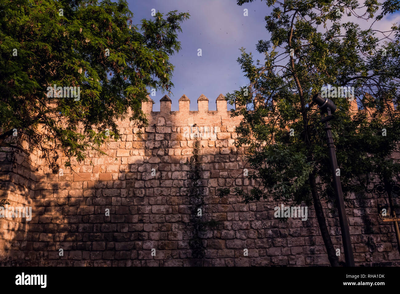 Battlement and sandstone wall with trees in the foreground and sky background Stock Photo