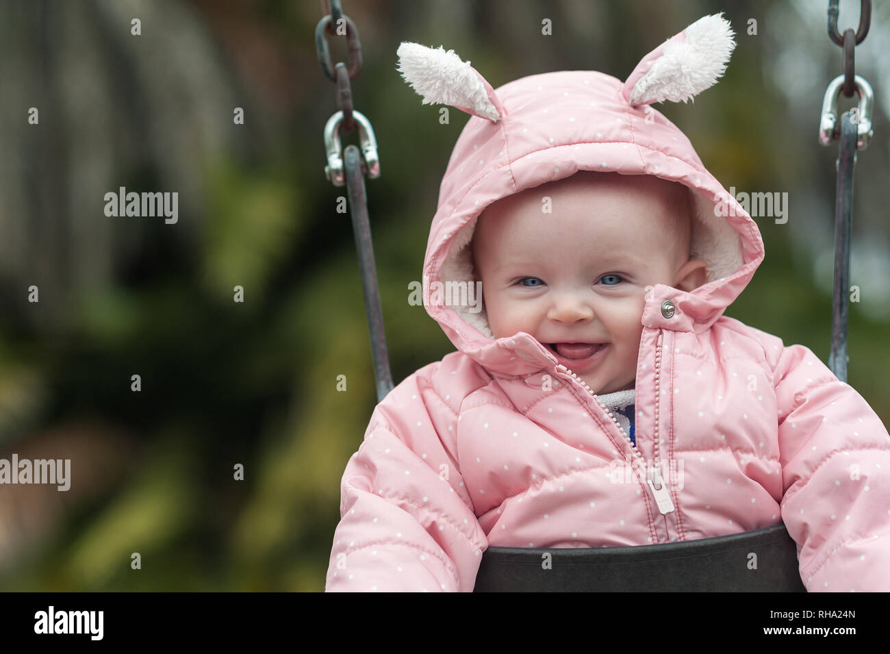 Close-up of a 6 month-old baby girl smiling on a swing during winter time at the Del Rey Lagoon Park in Playa Del Rey, CA. Stock Photo