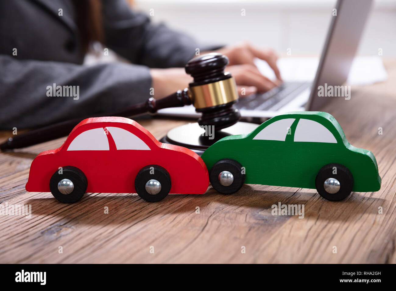 Small Green And Red Car In Front Of Gavel And Mallet And Businessperson Using Laptop Stock Photo