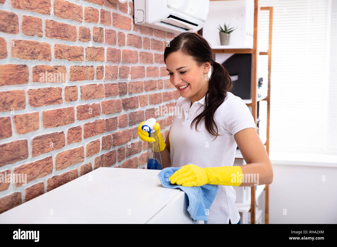 Smiling Young Woman Cleaning Furniture With Spray Bottle At Home Stock Photo