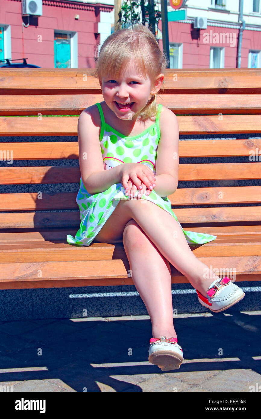 Little girl laughing while sitting on bench in city park. Positive children's emotions. Good mood. Child happy. Happy childhood. Child smiling. Enjoyi Stock Photo