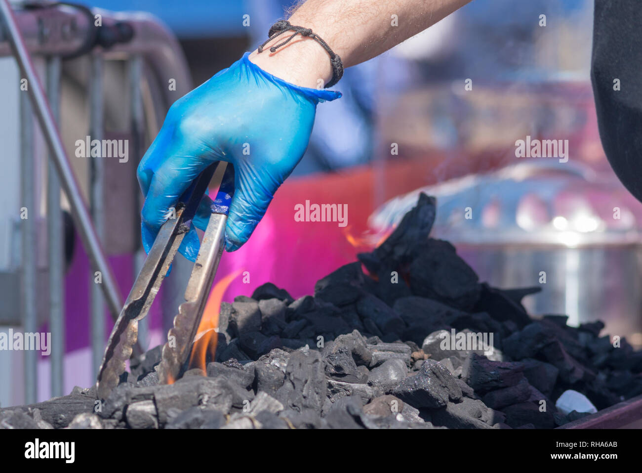 man wearing blue glove uses tools to move coals on barbecue Stock Photo Alamy
