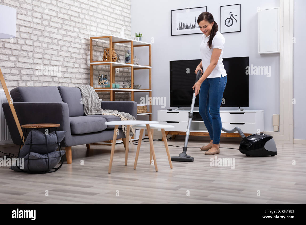 Happy Young Female Janitor Cleaning Floor With Vacuum Cleaner Stock