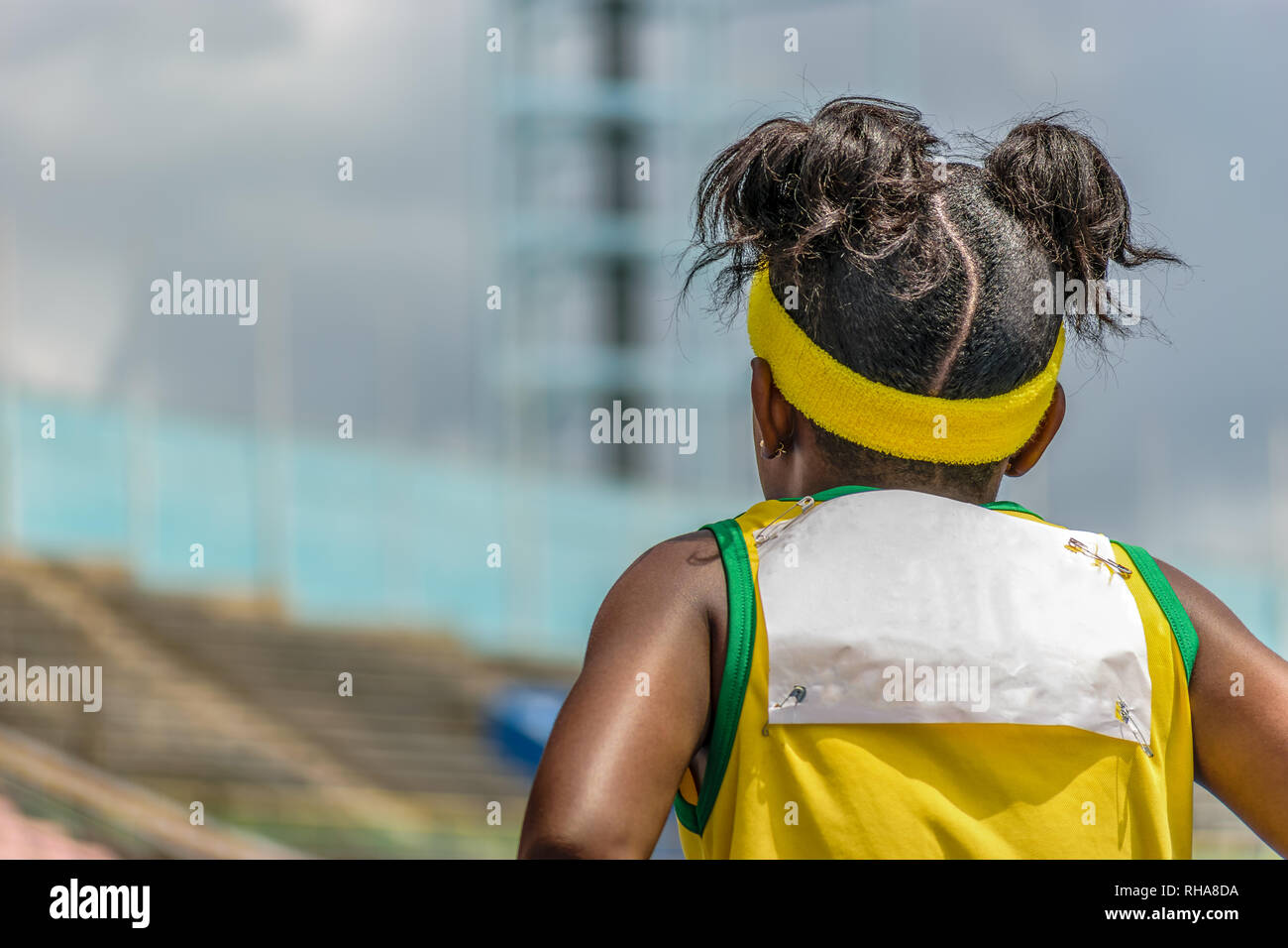Young black female child athlete wearing yellow and green jersey and headband in outdoor track and field stadium Stock Photo