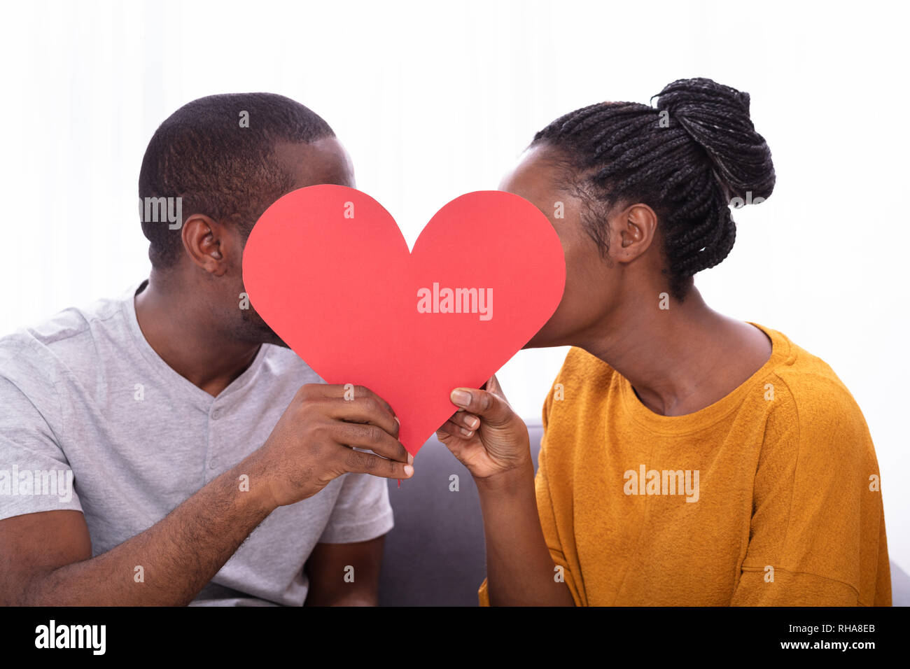 Close-up Of Young Couple Kissing Behind Red Heart Shape Stock Photo