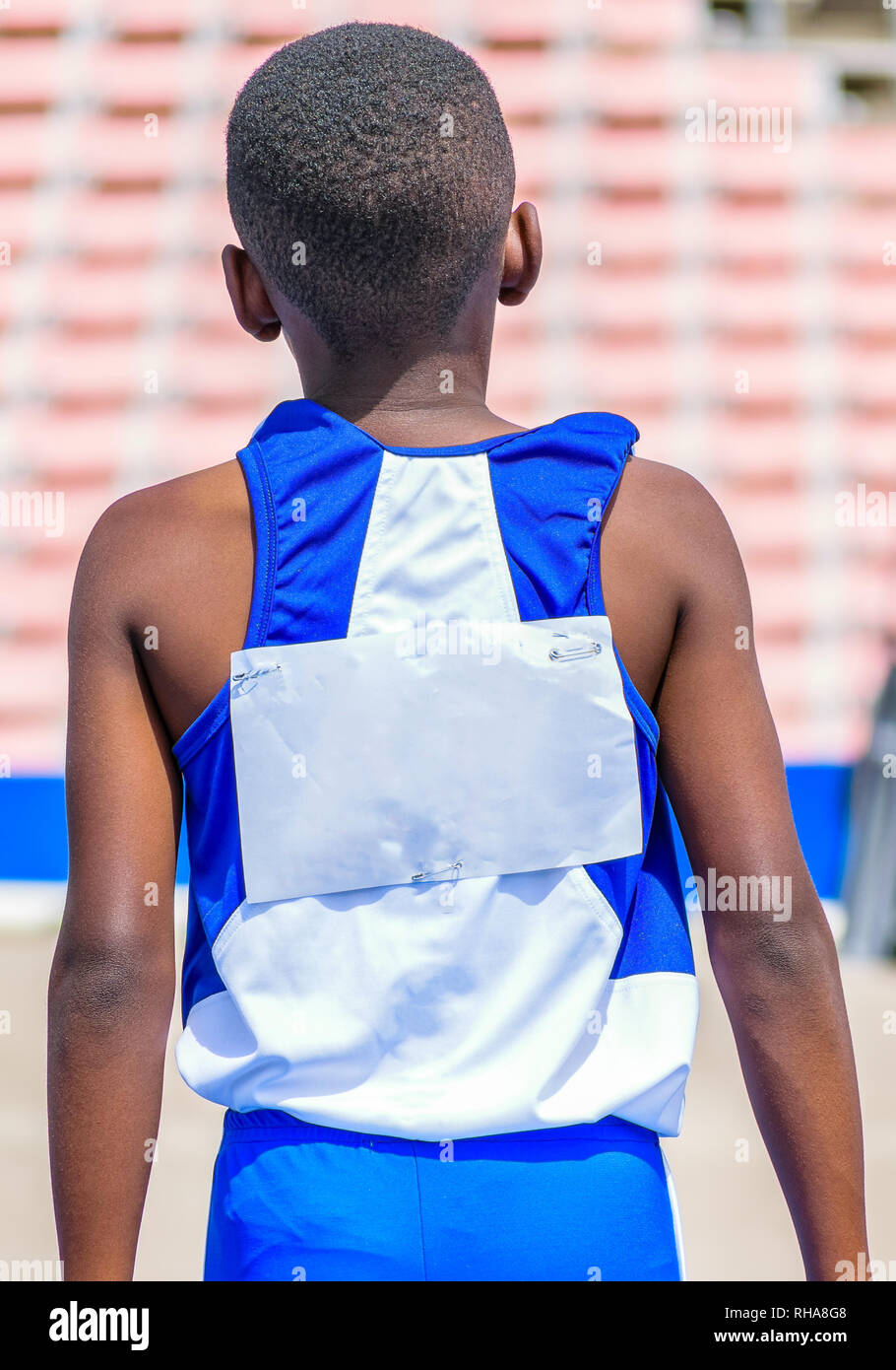 Young black male child athlete wearing blue and white jersey and shorts in outdoor track and field stadium Stock Photo
