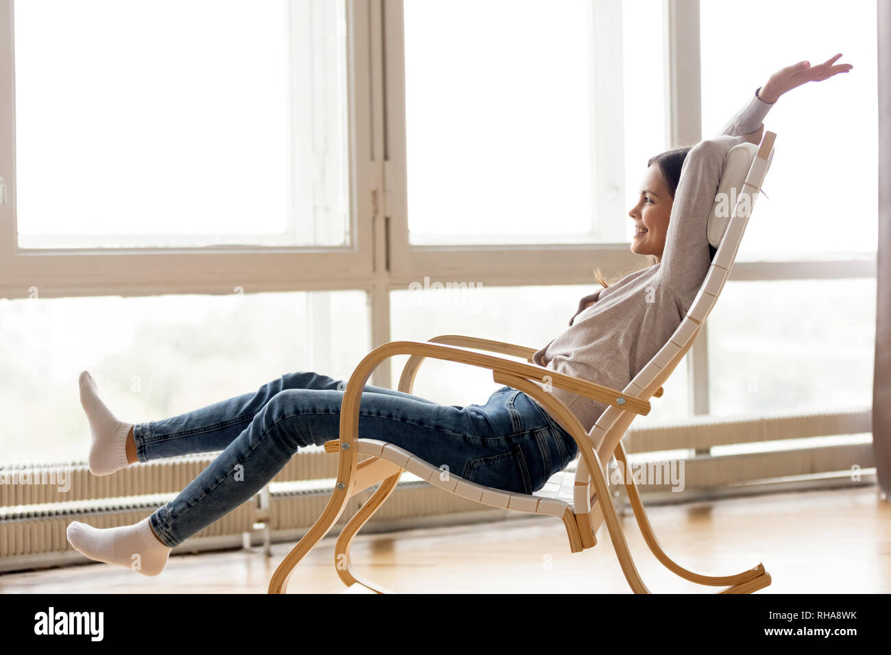 Carefree young woman relaxing on comfortable rocking chair at home Stock Photo