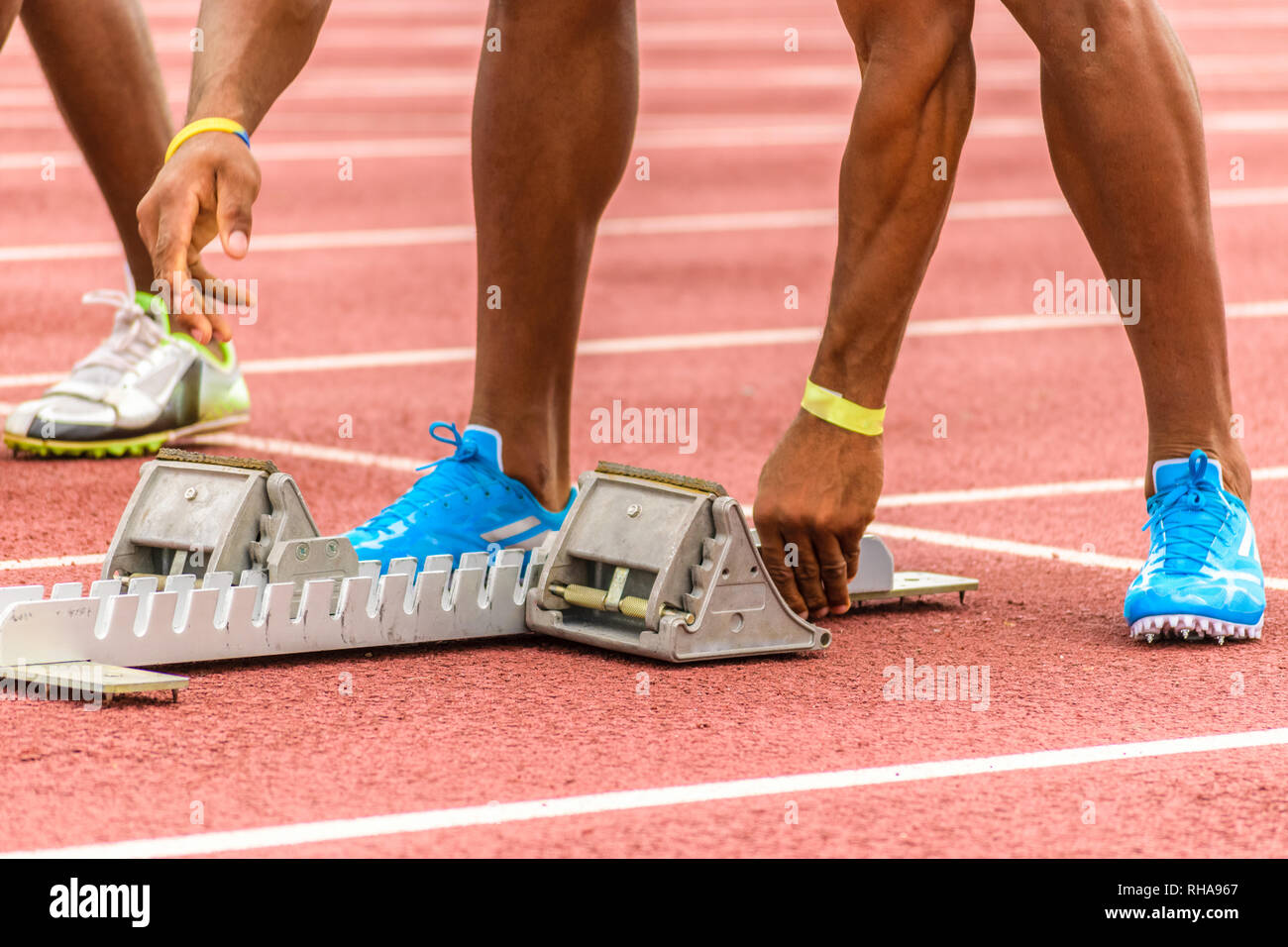 Starting blocks being adjusted by young black male athlete on outdoor track before start of race Stock Photo