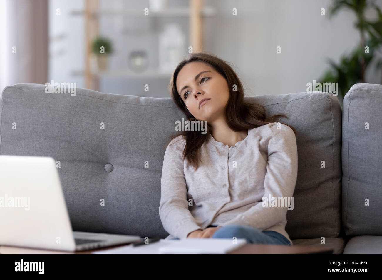 Tired apathetic teenager looking away sitting on couch feeling demotivated Stock Photo