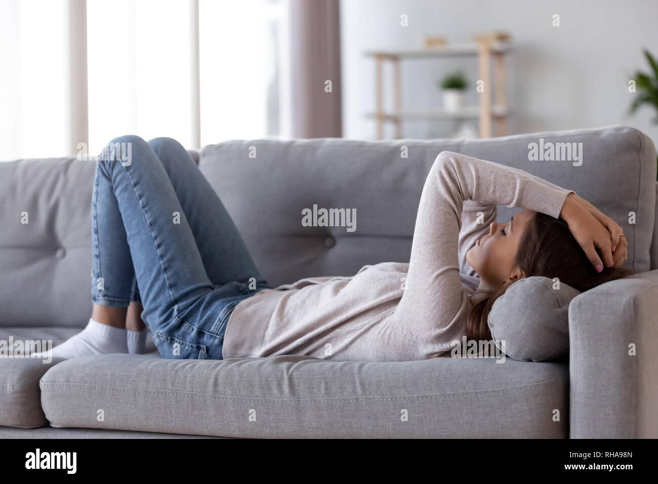 Sad depressed young woman lying on couch feeling headache  Stock Photo