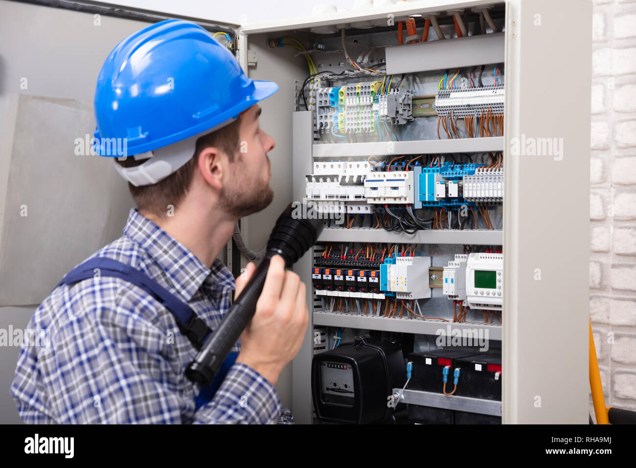 Close-up Of A Electrician Examining A Fuse Box With A Torch Stock Photo