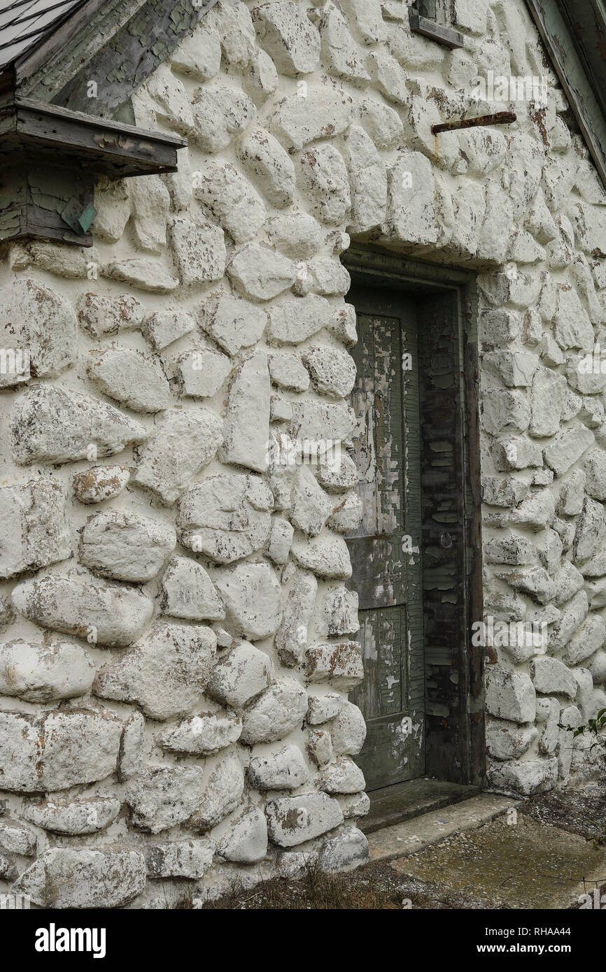 White stone building with old green doors and peeling paint. Old storage hut still used by the US Coast Guard, for Annisquam Lighthouse, Massachusetts Stock Photo