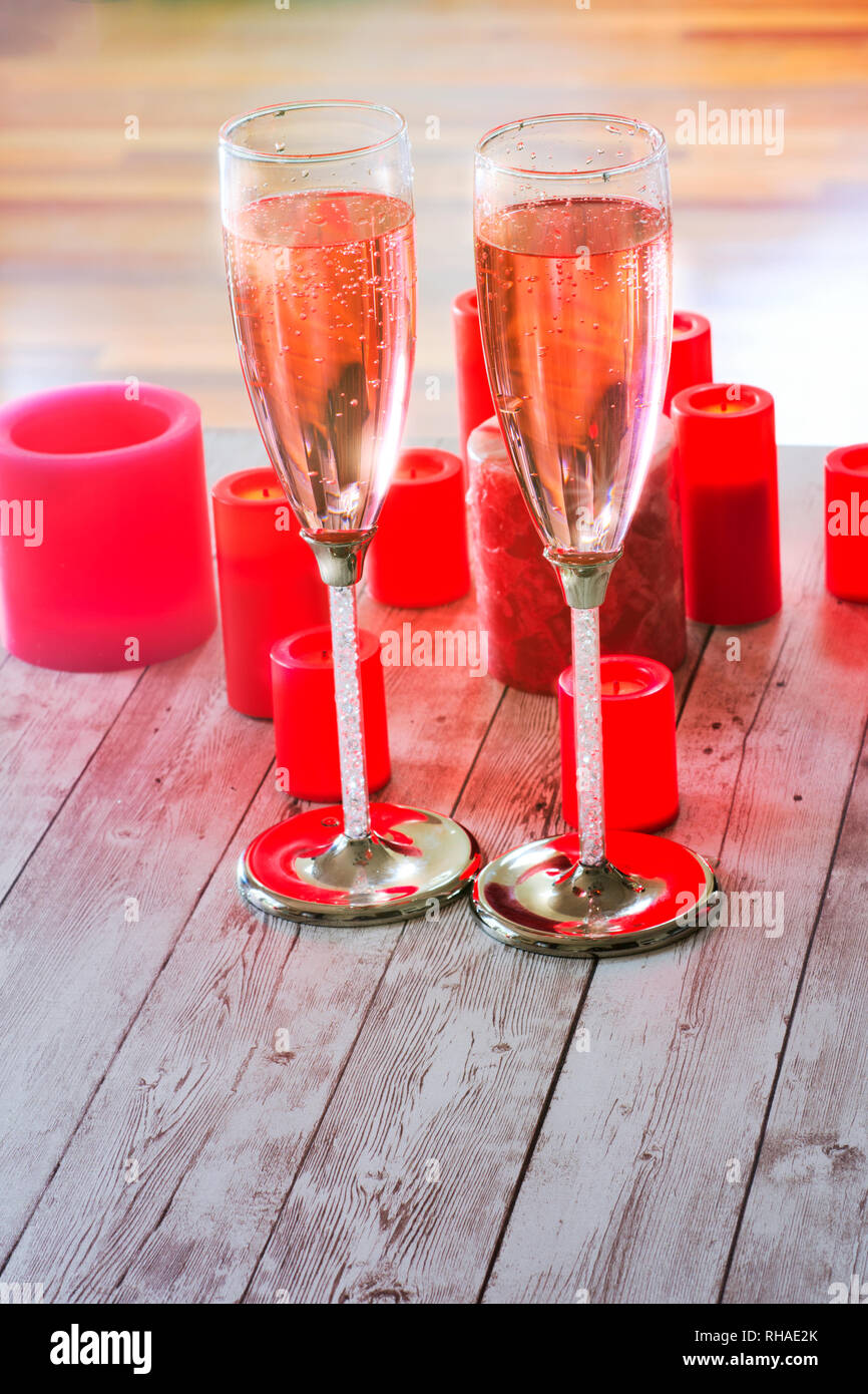 Two champagne flutes filled with pink bubbly beverage, on the tabletop surrounded with burning red candles. Stock Photo